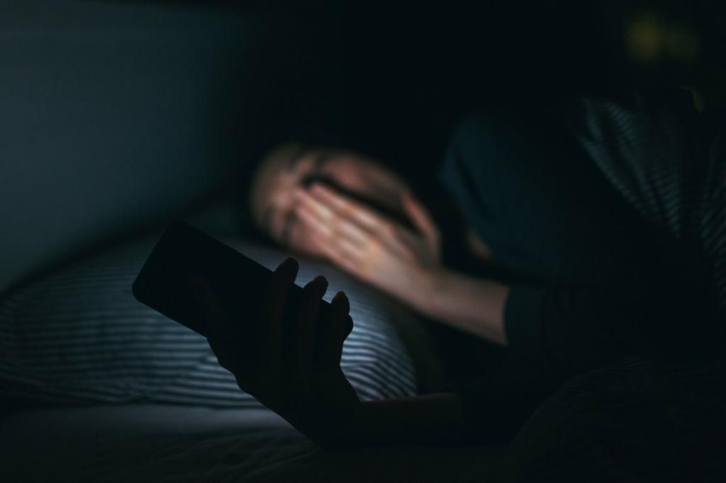 Tired woman yawning while using mobile phone on bed at night