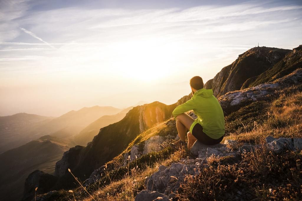 Italy, mountain running man sitting on rock looking at sunset