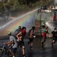 Demonstrators run as a riot police vehicle sprays water during a protest against Chilean President Sebastian Pinera's government in Santiago on January 10