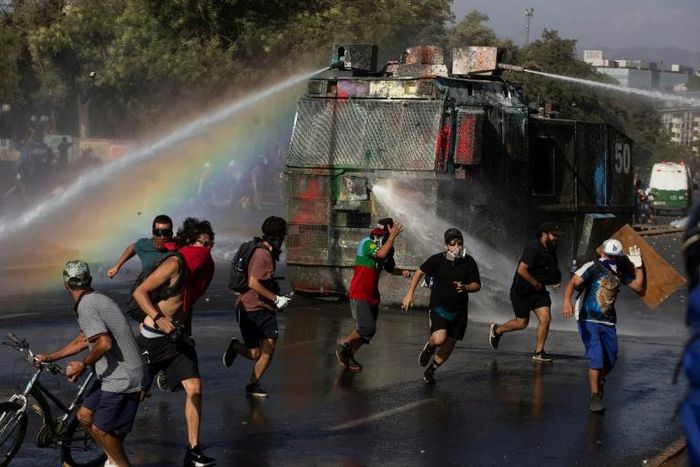 Demonstrators run as a riot police vehicle sprays water during a protest against Chilean President Sebastian Pinera's government in Santiago on January 10