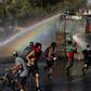 Demonstrators run as a riot police vehicle sprays water during a protest against Chilean President Sebastian Pinera's government in Santiago on January 10