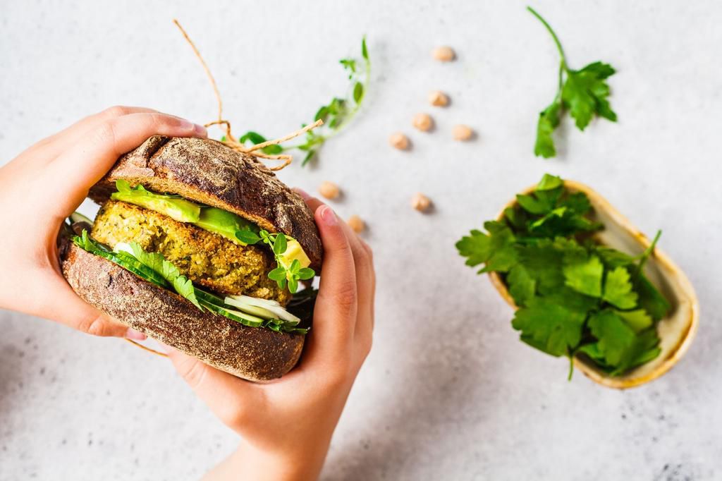 Vegan sandwich with chickpea patty, avocado, cucumber and greens in rye bread in children's hands.