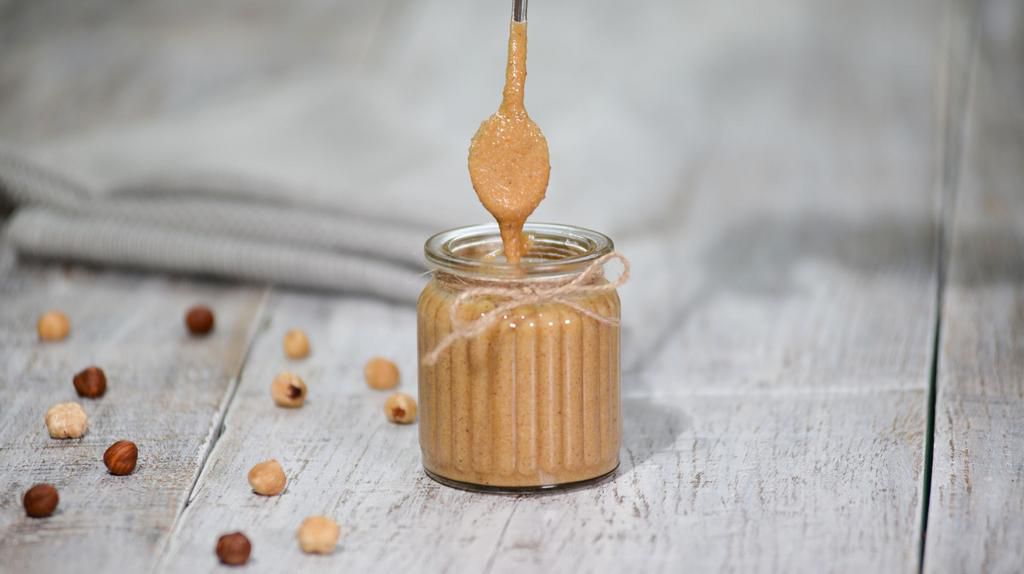 Hazelnut butter in a glass jar on a wooden table.