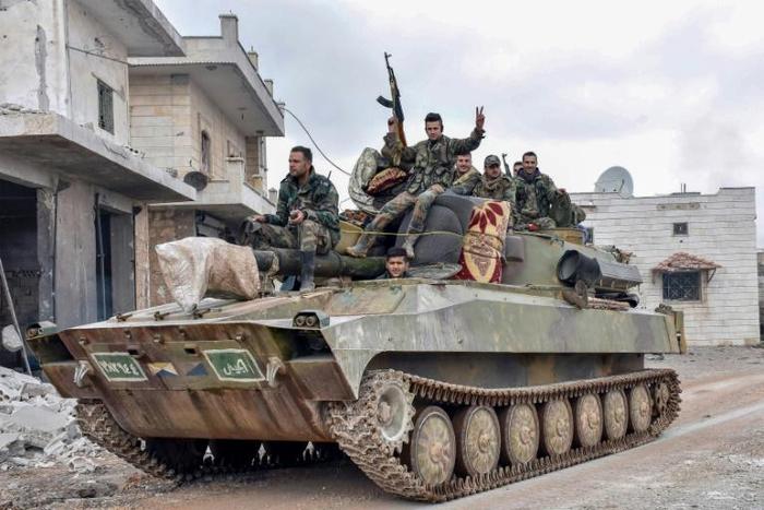 Syrian troops pass through a recaptured village in their final push on the strategic highway town of Maaret a-Numan, held by the rebels for seven years