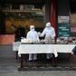 Restaurant workers wear protective clothing as they prepare food to sell on the street outside their restaurant in Beijing
