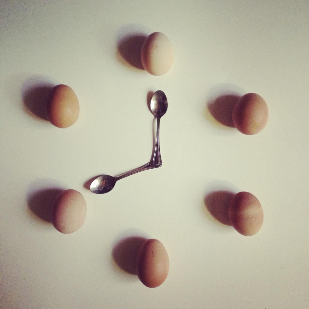Chicken eggs and two teaspoons arranged in form of clock face