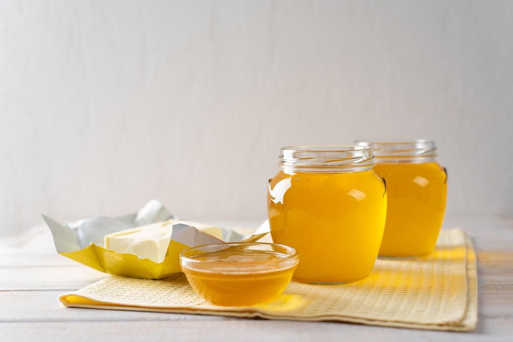 Hot homemade ghee butter in glass jars on a light background.