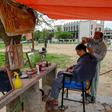 A barber wearing a facemask cuts a customer's hair at an open-air stall in Islamabad