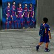 A boy wearing Barcelona's football kit looks at a poster depicting Lionel Messi and other players outside Camp Nou