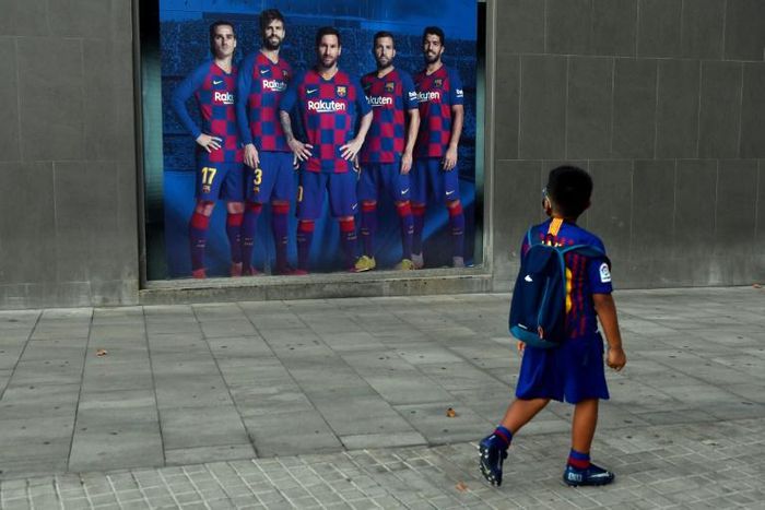 A boy wearing Barcelona's football kit looks at a poster depicting Lionel Messi and other players outside Camp Nou