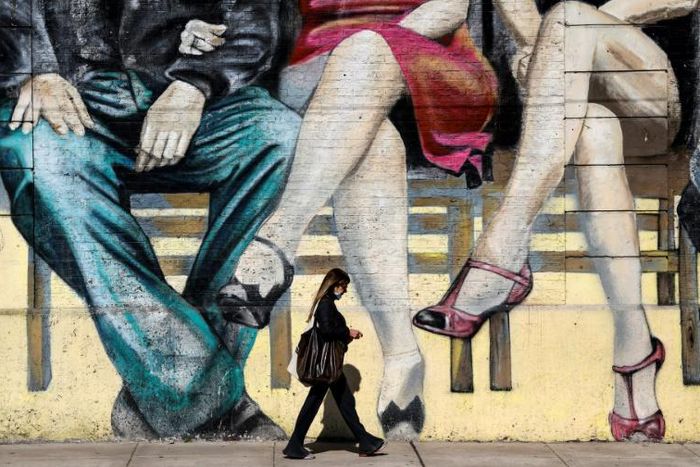 A woman walks past a mural featuring tango dancers in Buenos Aires