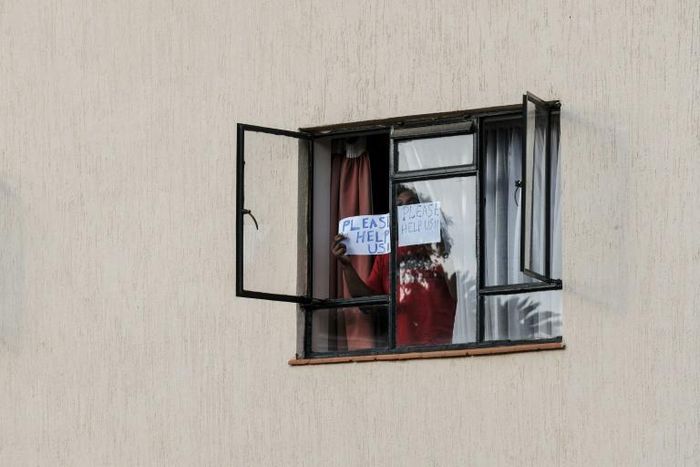 A man in mandatory quarantine in Kenya holds a sign reading "help me" out of the window of a facility in Nairobi