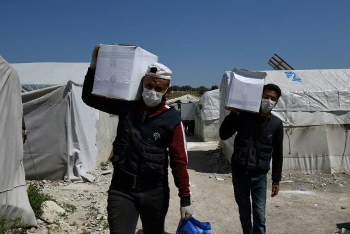 Volunteers deliver aid at a camp for displaced Syrians near the town of Deir al-Ballut, by the border with Turkey, in Syria's Afrin region in the northwest of the rebel-held side of the Aleppo province on April 14, 2020 during the coronavirus pandemic.