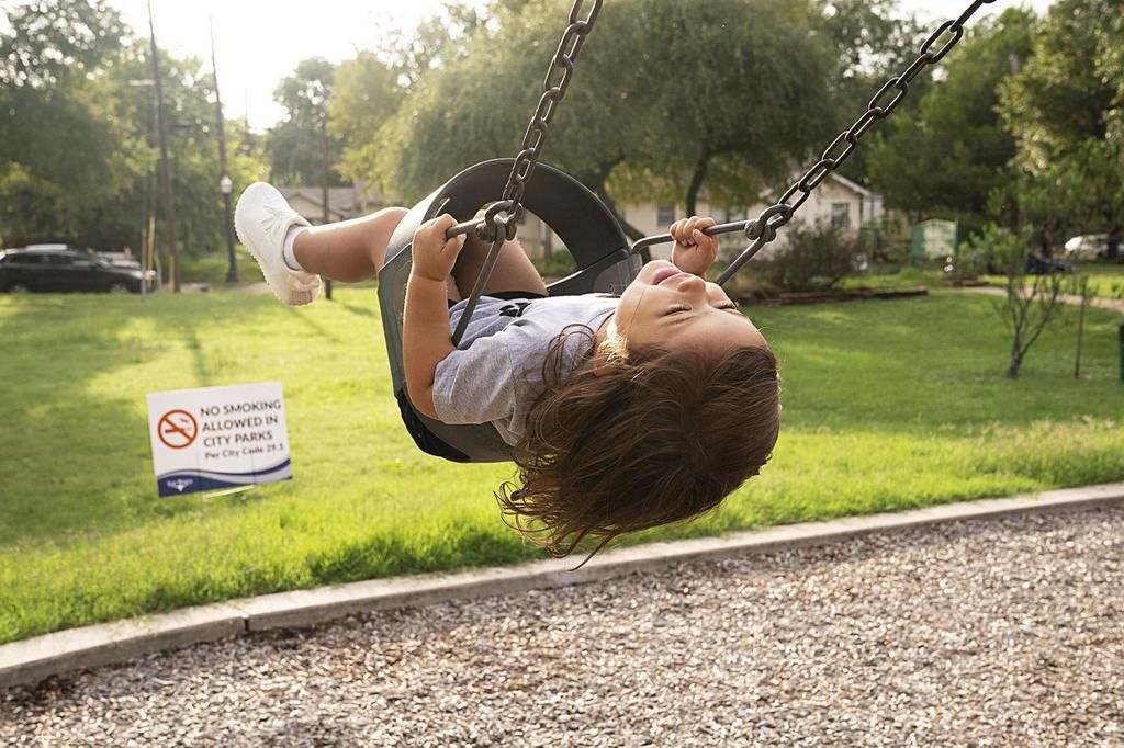 A child on a swing in Fort Worth, with a nearby sign indicating the ban on smoking in parks.