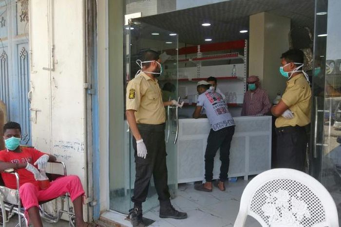 Mask-clad security guards and a patient at the entrance to al-Kubi hospital in Yemen's southern coastal city of Aden