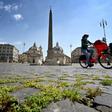 Grass grows between cobblestones as a woman rides a bicycle across Piazza del Popolo on April 24, 2020 in Rome, during the country's lockdown aimed at stopping the spread of the COVID-19 pandemic, caused by the novel coronavirus