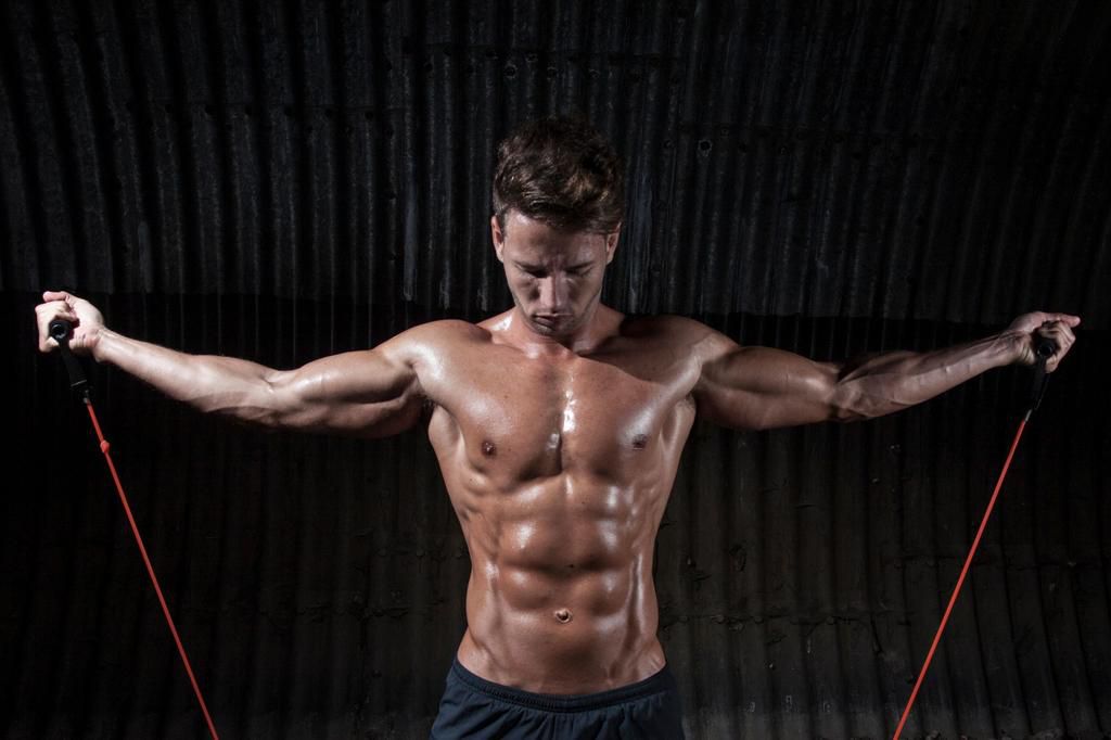 Macho Man Exercising With Resistance Bands Against Corrugated Iron