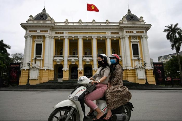 Women wearing face masks ride past the Opera House in Hanoi on April 23, 2020, as Vietnam eased its nationwide social isolation effort to prevent the spread of the COVID-19 novel coronavirus. Vietnam eased social distancing measures on April 23, with e...