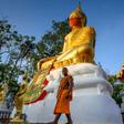 A monk walks in front of a giant Buddha statue wearing a face mask at Wat Nithet Rat Pradit temple in Pathum Thani outside Bangkok