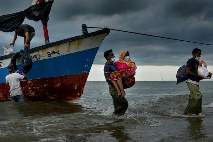 Acehnesse fishermen help carry a Rohingya child ashore after locals defied authorities who didn't want the asylum seekers to land