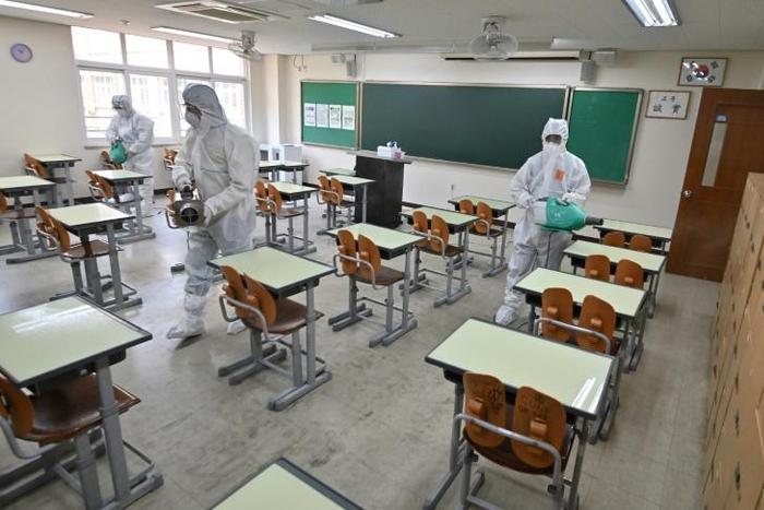 Health officials wearing protective gear spray disinfectant in a classroom at a high school in Seoul