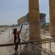 A worker (pictured May 18, 2020) wearing a protective mask cleans a divider made of plexiglass at the entrance of the Acropolis in Athens amid the pandemic of the novel coronavirus