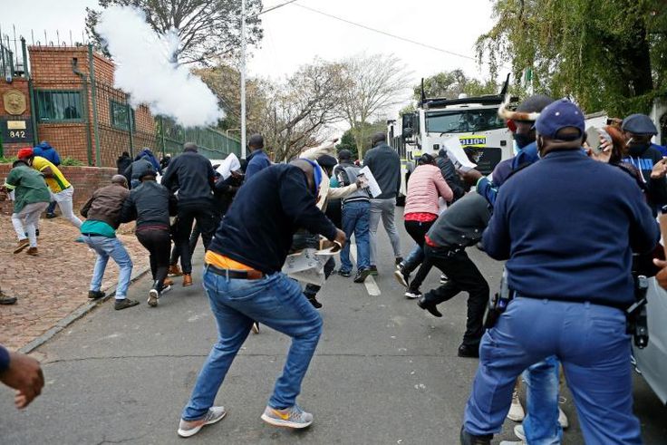 Protesters run from a stun grenade fired by police outside the Zimbabwean Embassy in South Africa's Pretoria