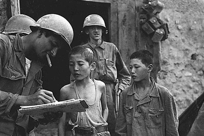 Two boys serving in the North Korean Army are interrogated by a US soldier after they were taken prisoner