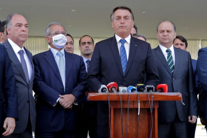 Brazilian President Jair Bolsonaro (C) speaks alongside Brazilian Economy Minister Paulo Guedes (L), deputies and senators during a statement on financial aid for vulnerable Brazilians amid the COVID-19 pandemic, at Planalto Palace, in Brasilia