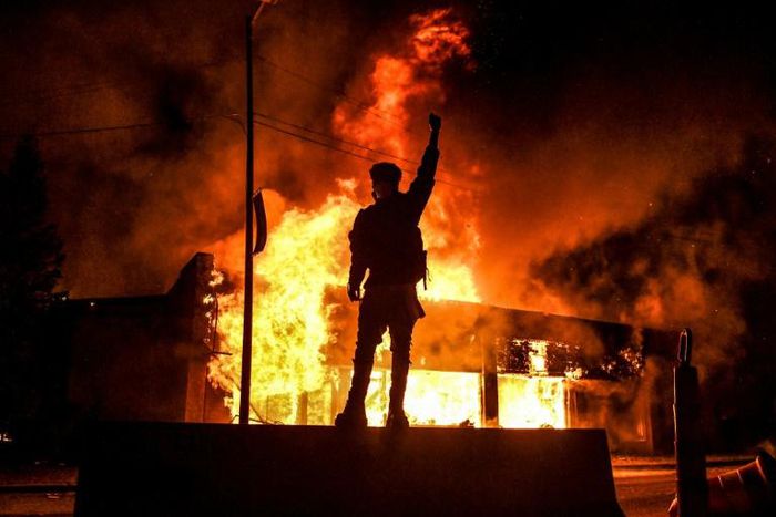 Un manifestant devant un bâtiment incendie dans la ville américaine de Minneapolis dans la nuit du 29 au 30 mai 2020