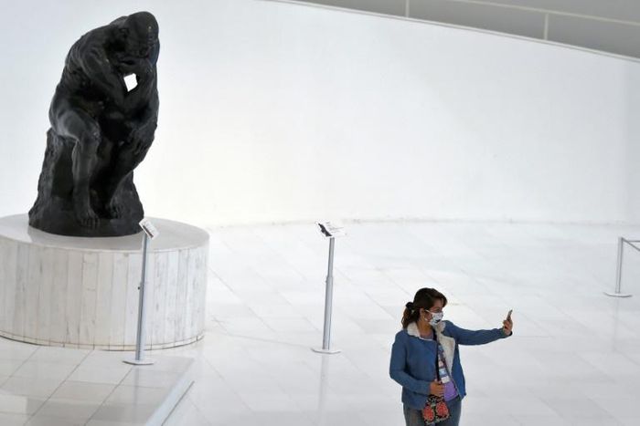 A visitor -- wearing a face mask -- takes a selfie at the Soumaya Museum in Mexico City in front of a Rodin sculpture