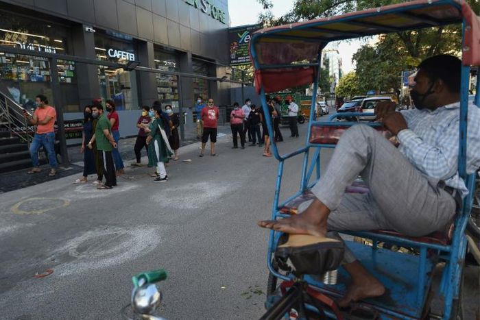 A rickshaw puller wearing a face mask watches people standing in a queue in New Delhi on April 8. Officials have now made wearing a mask in the Indian capital compulsory