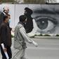 A man wearing a facemask against coronavirus walks past a wall painted with images of US Special Representative for Afghanistan Reconciliation Zalmay Khalilzad and Taliban co-founder Mullah Abdul Ghani Baradar, in Kabul