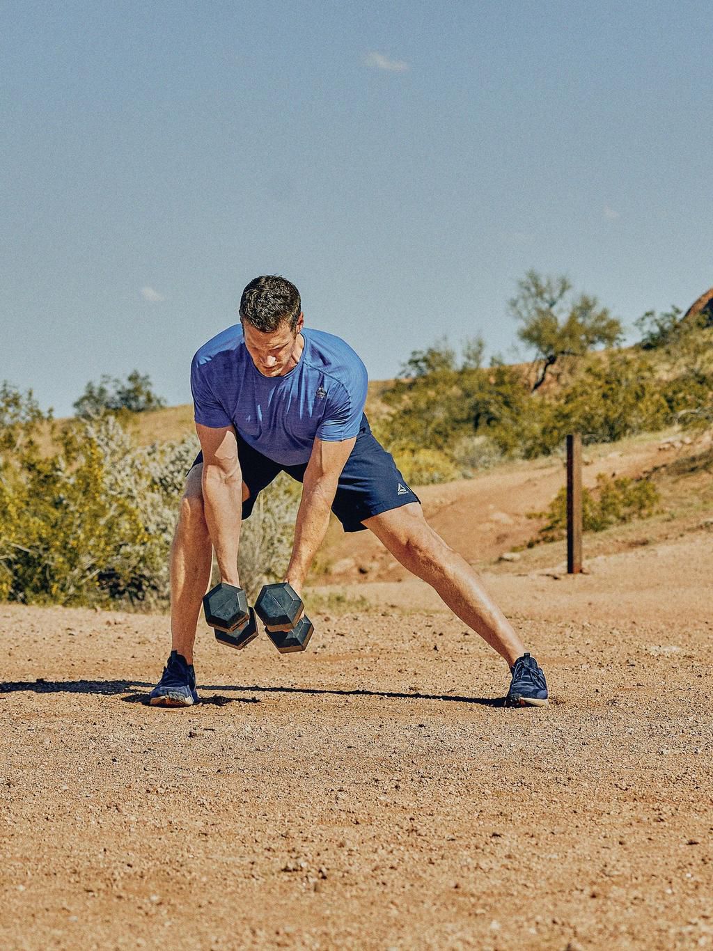 man in offset straddle position, both dumbbells lowered from a row position