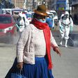 A woman dressed in typical indigenous clothing walks near municipal employees disinfecting the streets of Puno in Peru