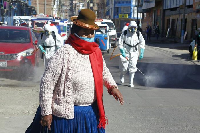 A woman dressed in typical indigenous clothing walks near municipal employees disinfecting the streets of Puno in Peru