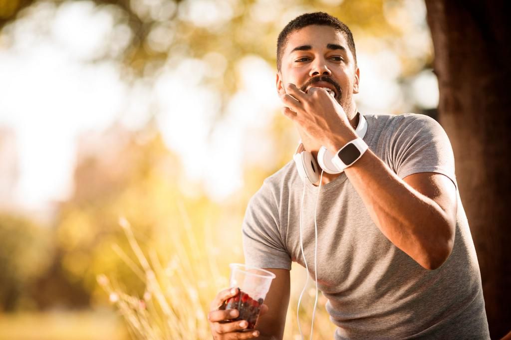 Active young sportsman having a cup of berries after an exercise in a city park