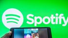 Someone holds a tablet featuring a Spotify playlist in front of Spotify logo background.