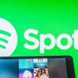 Someone holds a tablet featuring a Spotify playlist in front of Spotify logo background.