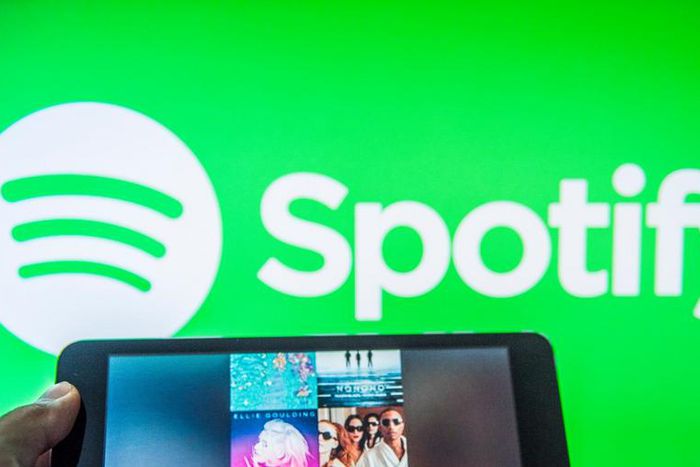 Someone holds a tablet featuring a Spotify playlist in front of Spotify logo background.