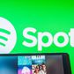 Someone holds a tablet featuring a Spotify playlist in front of Spotify logo background.