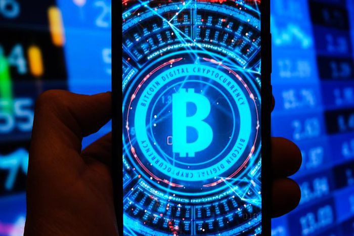 A multiple exposure image shows a Bitcoin logo displayed on a smartphone with stock market percentages in the background