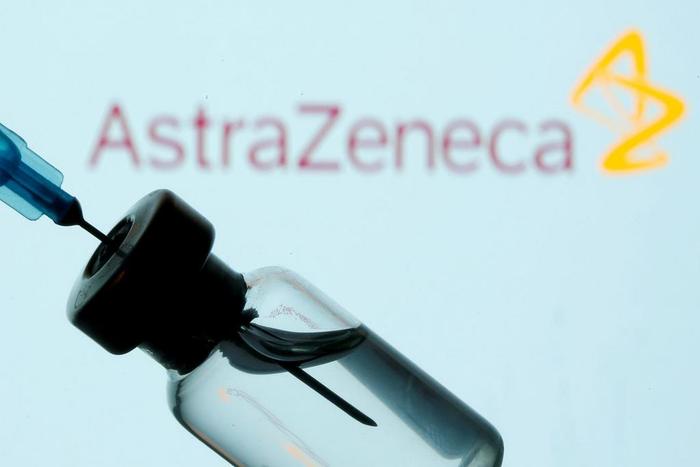 A vial and syringe are seen in front of the AstraZeneca logo.