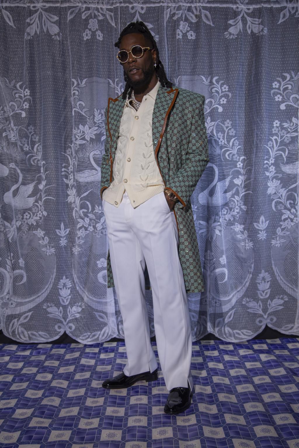 Burna Boy wears a Gucci coat,  Casablanca knit top, Loius Vuitton trousers, Christian Louboutin shoes and the sunglasses, watch and jewellery are from his personal collection