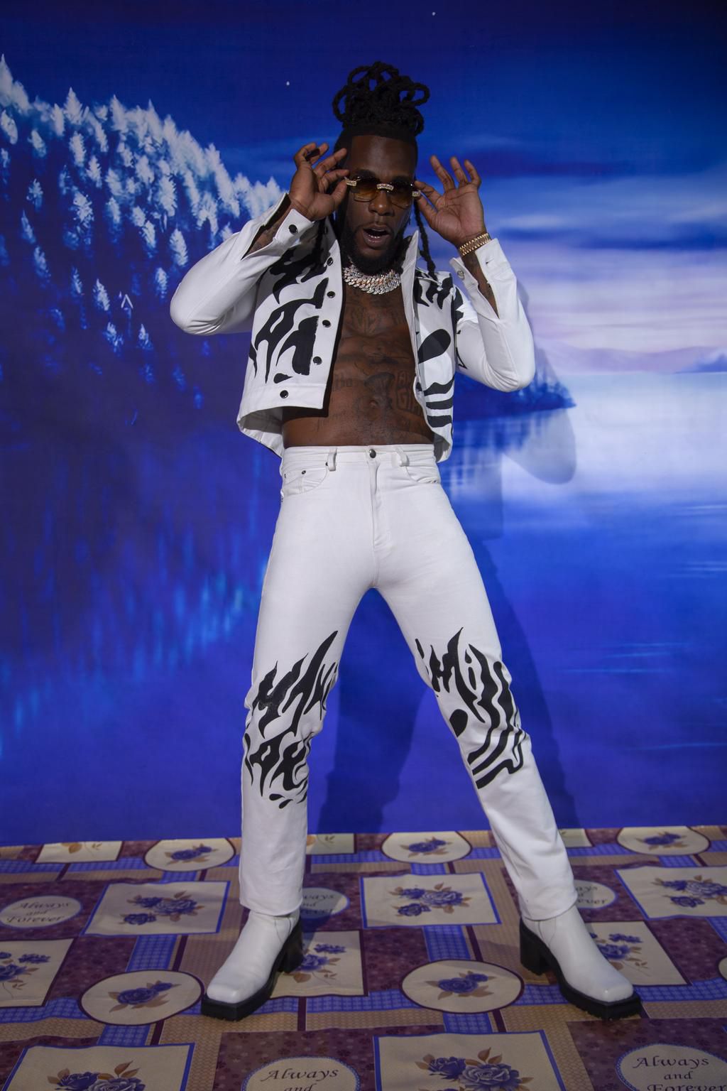 Burna Boy wears a maximillian jacket, trousers from brownsfashion.com., John Lawrence Sullivan boots and his personal jewellery and sunglasses