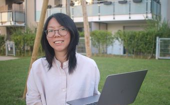Melody Koh standing on grass and holding her laptop.