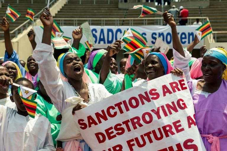 Demonstrators chant slogans and wave Zimbabwe's national flag during a rally to denounce US and EU economic sanctions