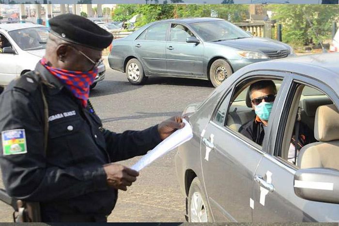 A Nigerian police officer checking a vehicle documents at a checkpoint. [Carmart]
