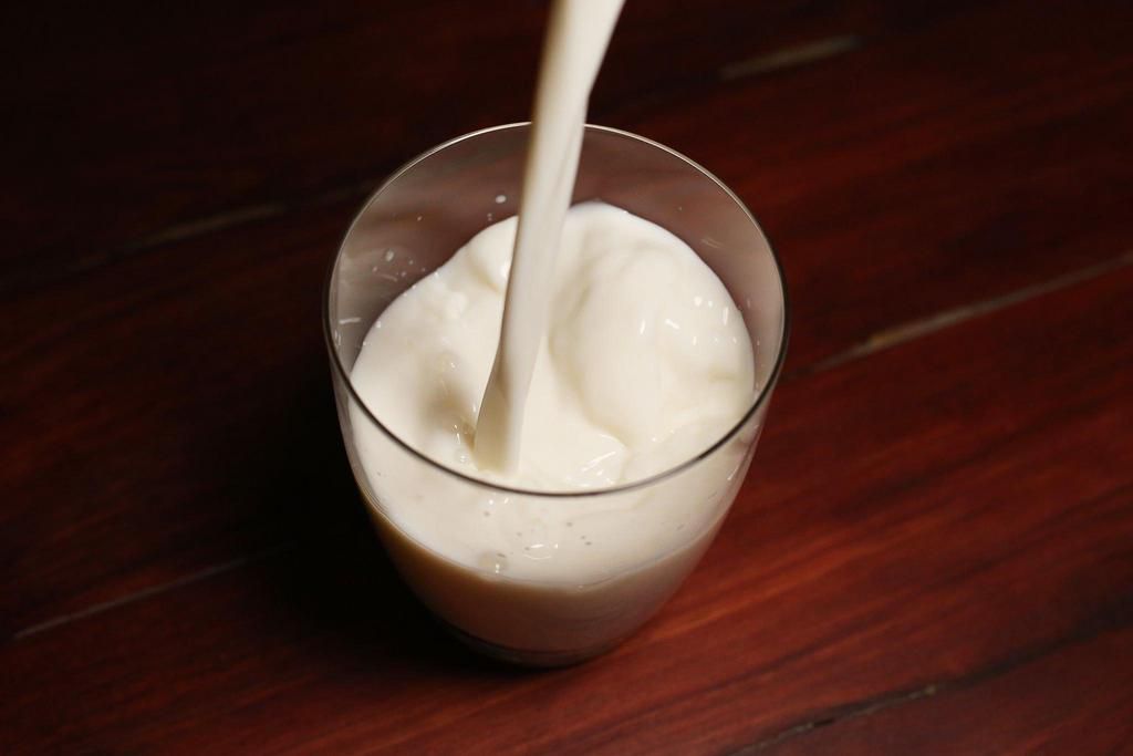 A jar of milk being poured into a glass cup