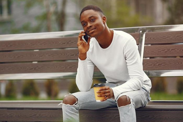 A young man using his phone while sitting on a park bench [Image: Gustavo Fring]